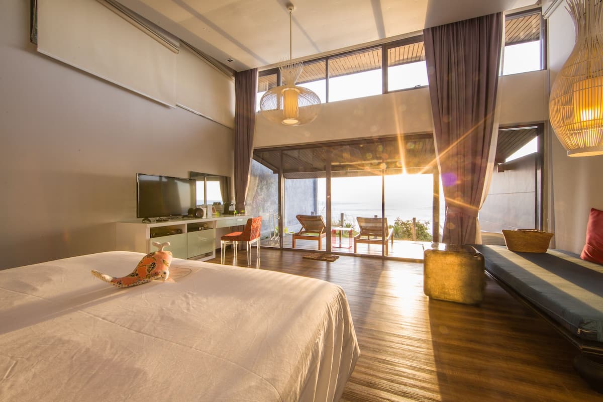A spacious bedroom with a large bed, a desk, a television, and a view of the outdoors.