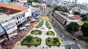 A plaza with a central open space surrounded by buildings, a crosswalk, and a road with vehicles. - Hotel República (Panama City)