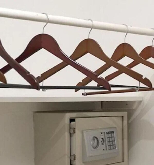 Un depósito seguro con cerradura numérica, ubicado debajo de una barra metálica con perchas de madera.