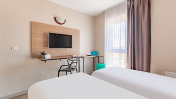 Una camera d'albergo con due letti, una scrivania con televisore, una piccola pianta e una valigia.