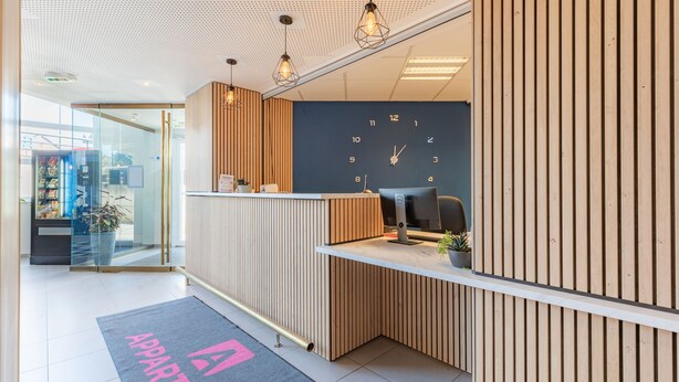 Una zona de recepción con un reloj, paneles de madera, un mostrador y una planta.