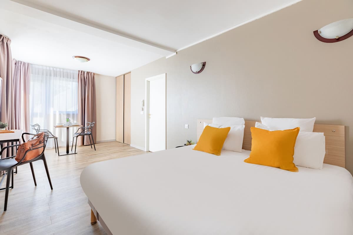 Une chambre d’hôtel avec un grand lit, deux oreillers, un bureau avec une chaise et une fenêtre avec des rideaux.