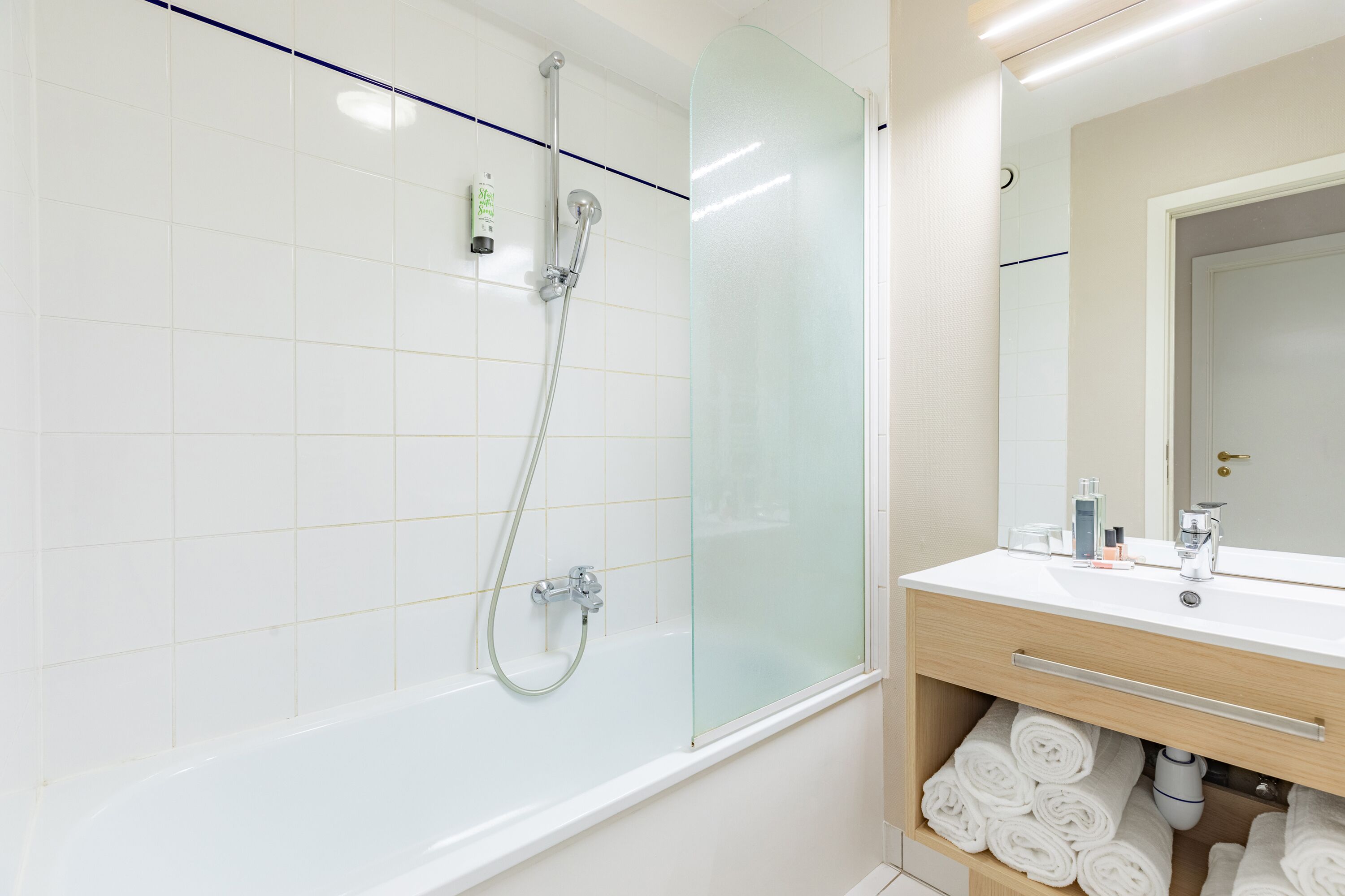 A modern bathroom with a glass-enclosed shower, a white sink with a mirror, and neatly folded towels.