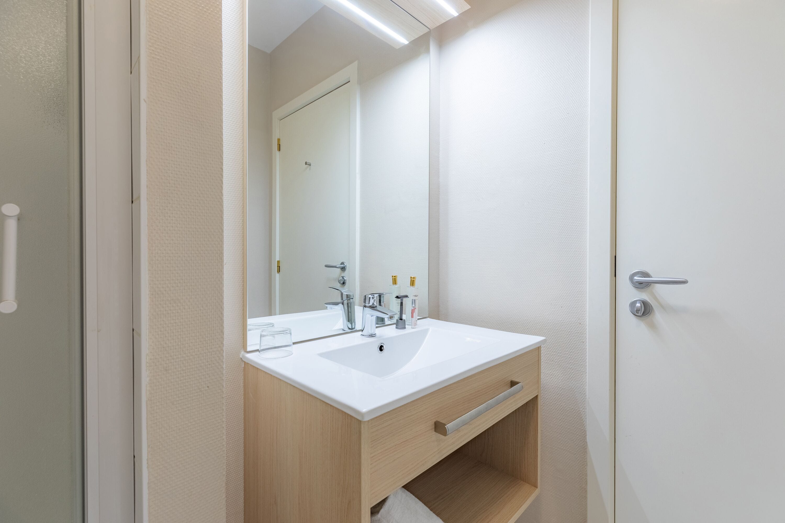 Ein modernes Badezimmer mit einem weißen Waschbecken, einer Holzkommode und einem Spiegel.