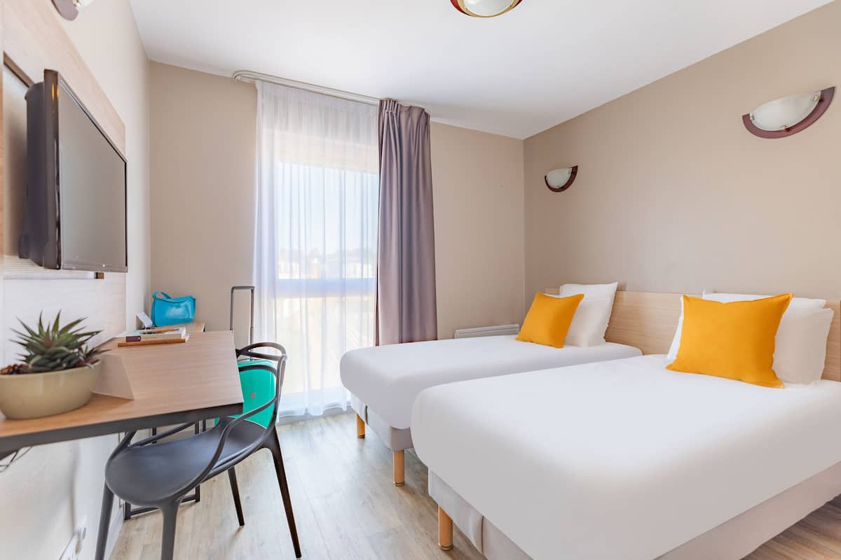 Une chambre d’hôtel avec deux lits, un bureau avec une chaise, une télévision et une fenêtre avec des rideaux.