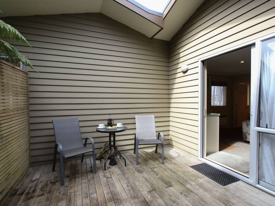 A covered patio with a table and two chairs, a wooden floor, and a sliding glass door leading to an interior room.
