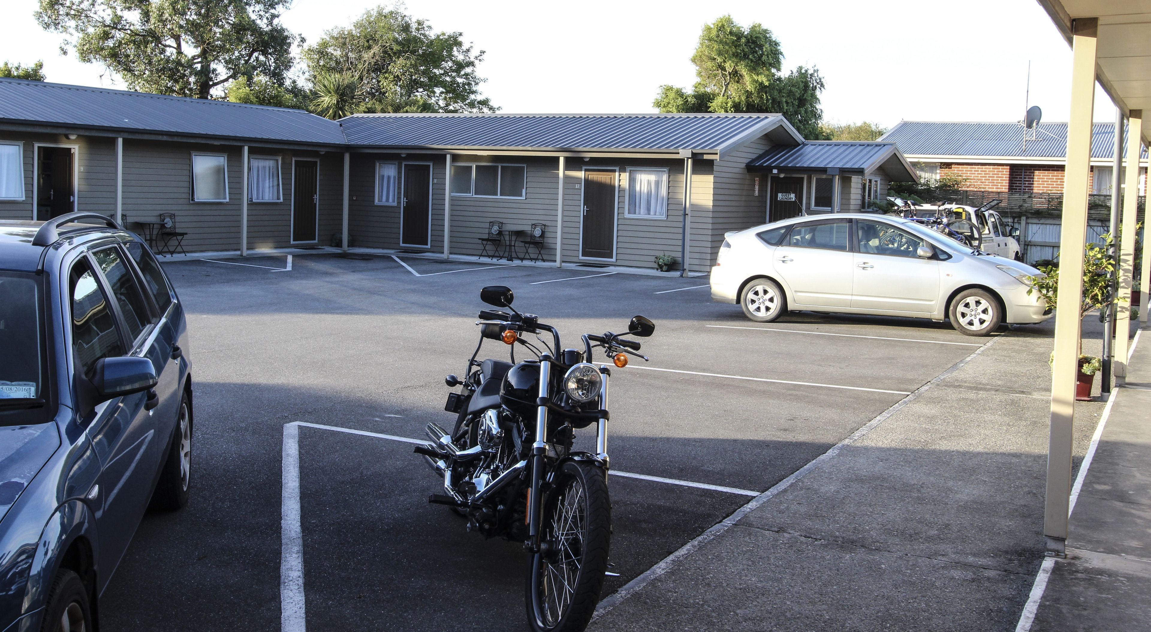 En parkeringsplats med en motorcykel och en bil, en byggnad med flera rum och en satellantenn på taket.