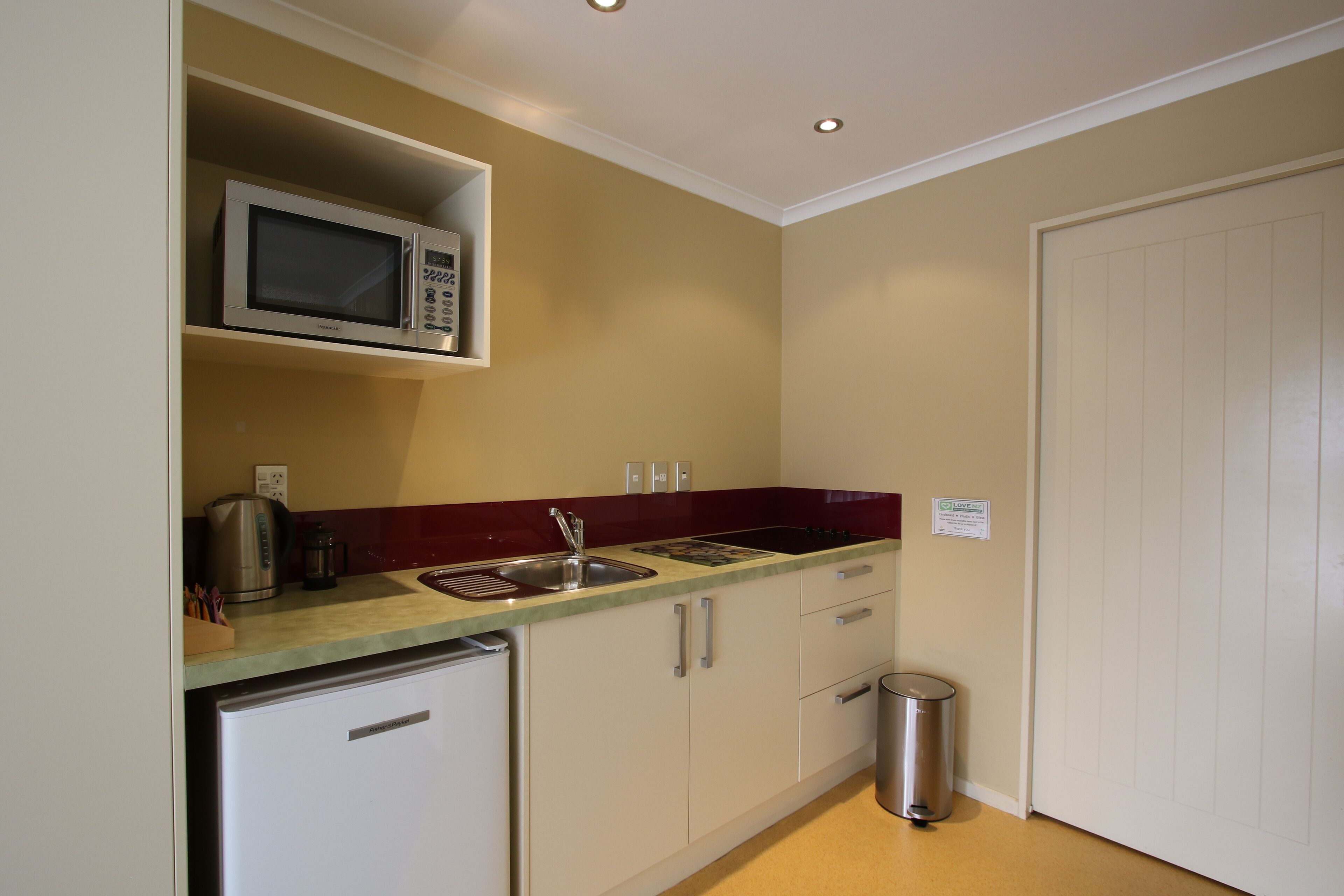 A compact kitchen with a microwave, sink, and a small trash bin.