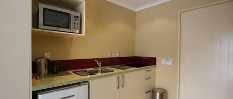 A compact kitchen with a microwave, sink, and a small trash bin.