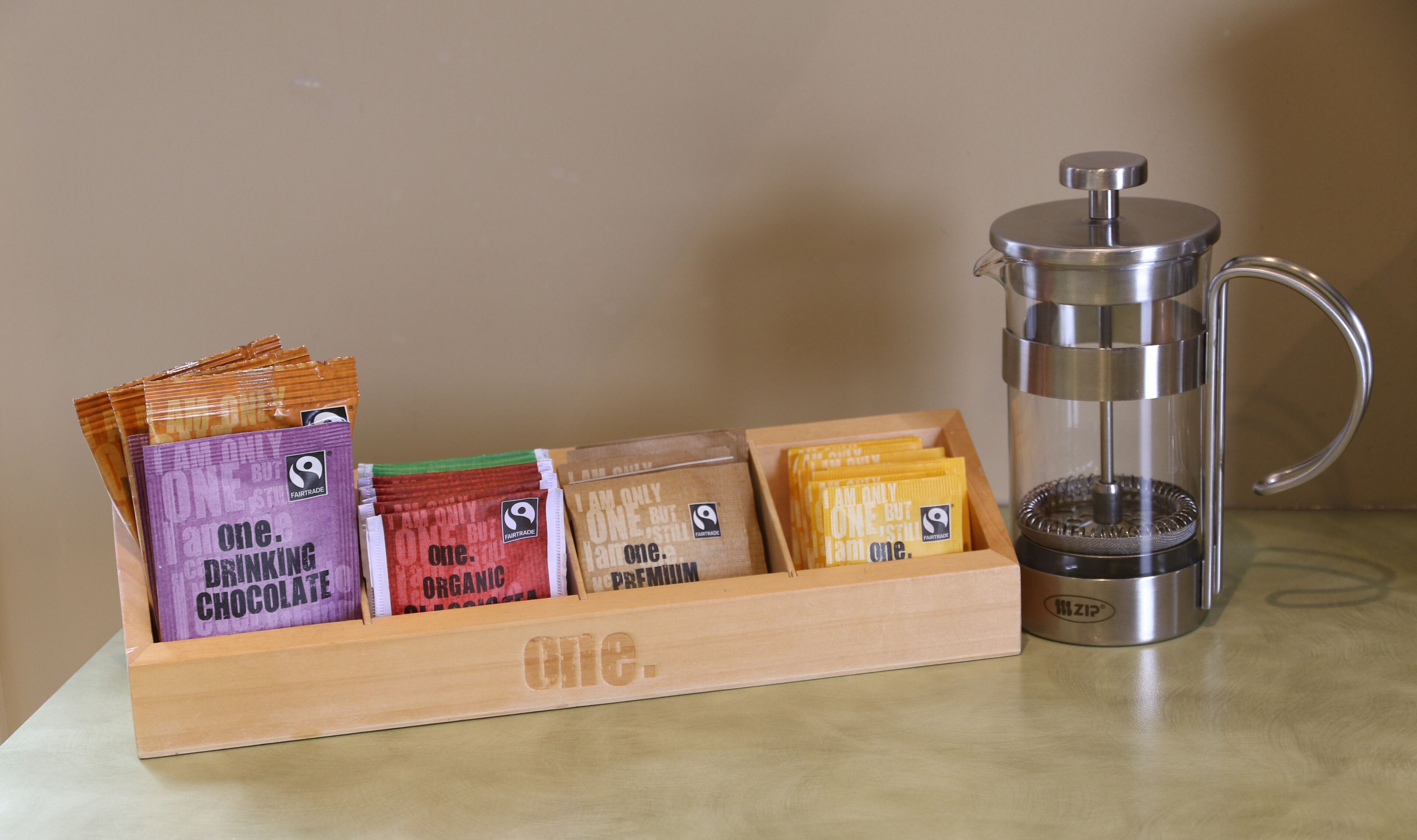 A wooden box with coffee pods and a stainless steel coffee press on a table.