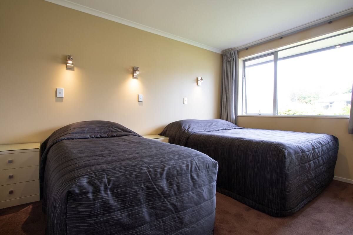 A bedroom with two beds, a nightstand, and a window with curtains.