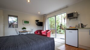 A bedroom with a large bed, a desk, a red chair, a television, a microwave, and a small refrigerator. - Annabelle Motel (Hokitika)