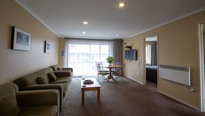 A living room with a sofa, a coffee table, and a dining table with chairs. There is a plant on the dining table. - Annabelle Motel (Hokitika)