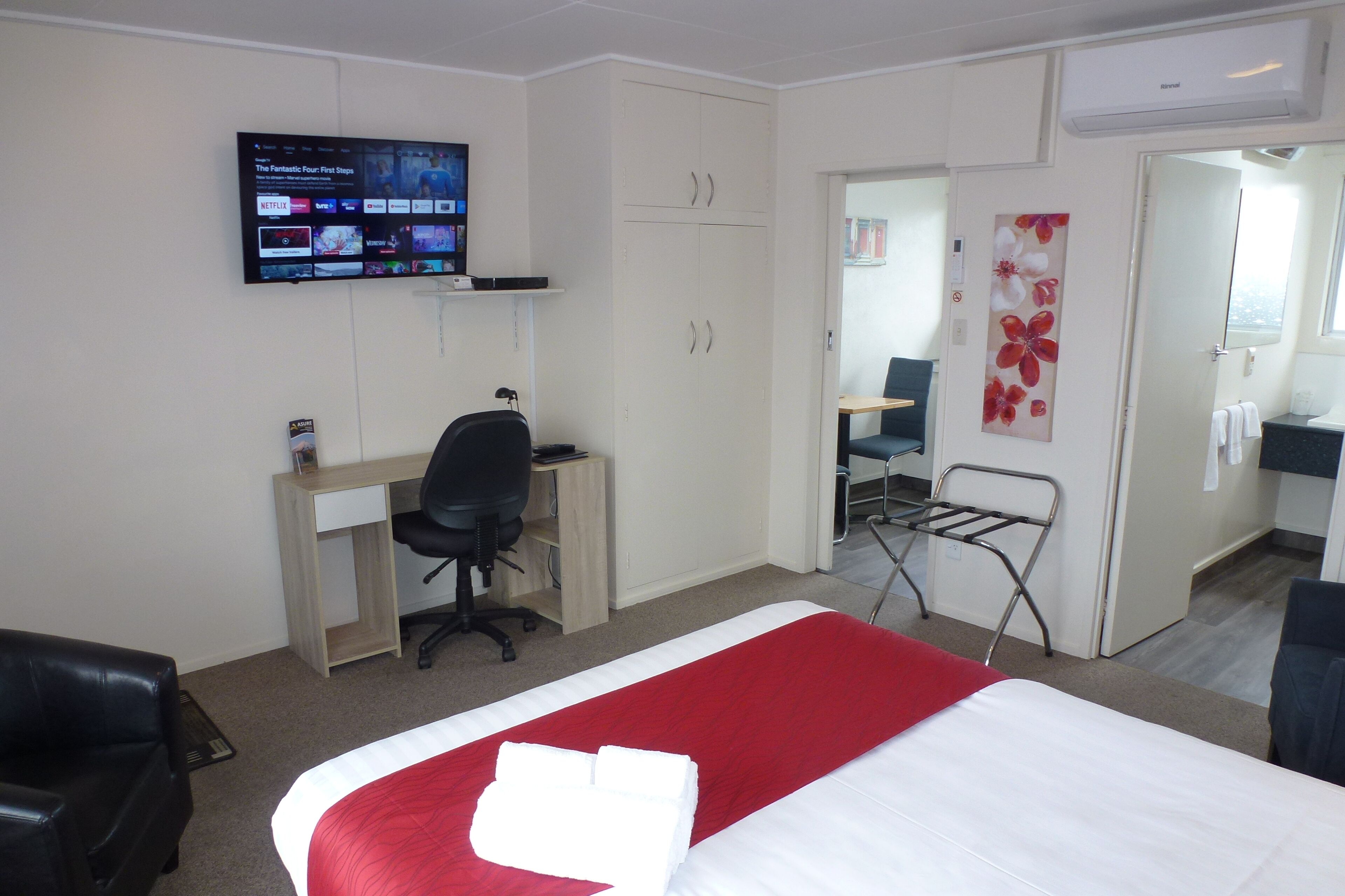 Hotelkamer met een bed, een bureau, een stoel, een aan de muur bevestigde televisie en een badkamer door een open deur zichtbaar.