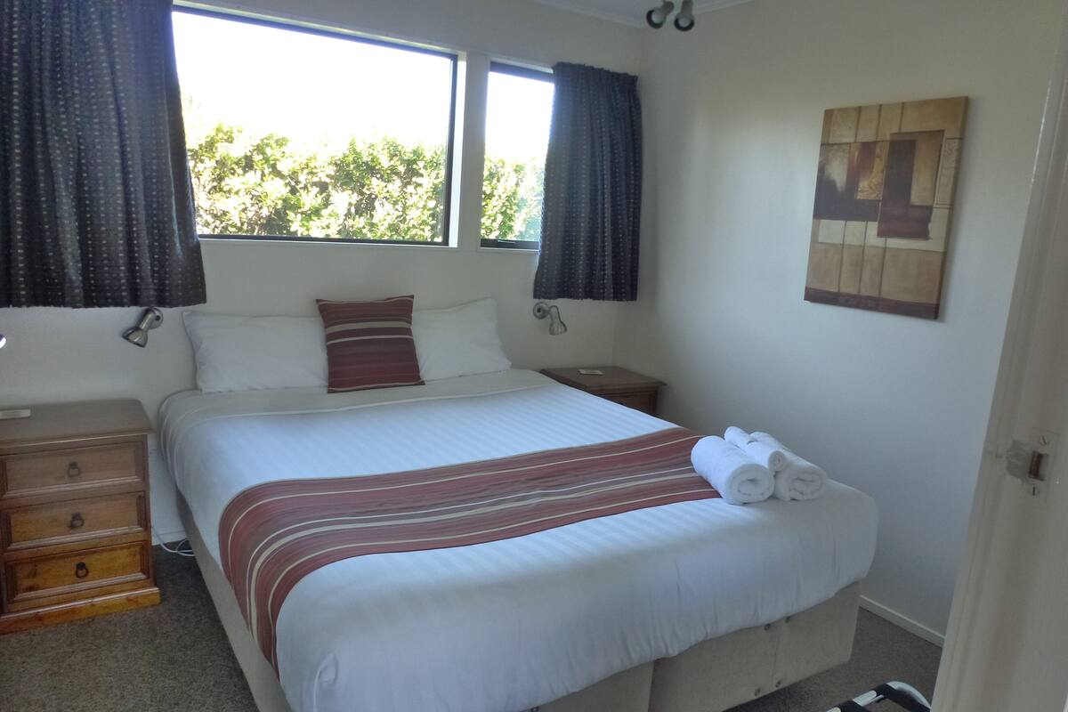 A neatly made bed with a striped bedspread, two bedside tables, a nightstand, and a wall-mounted artwork.