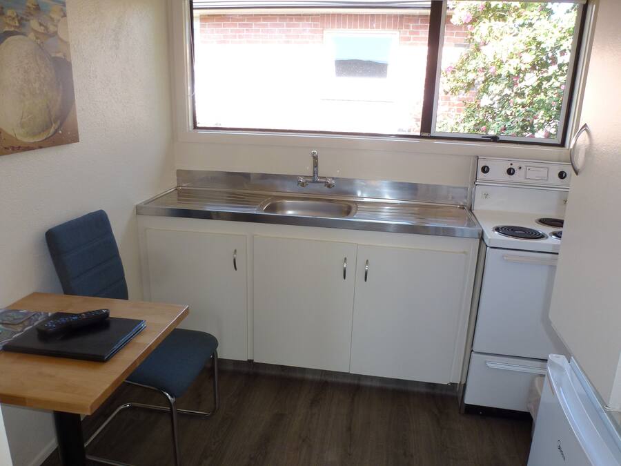 Cocina compacta con lavamanos, estufa y ventana que ofrece vistas a una pared de ladrillo y vegetación.