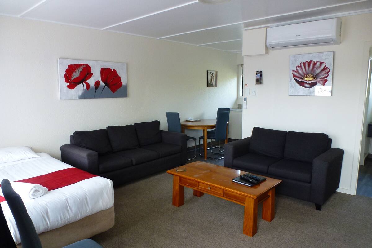 A hotel room with a bed, two sofas, a coffee table, and artwork on the walls.