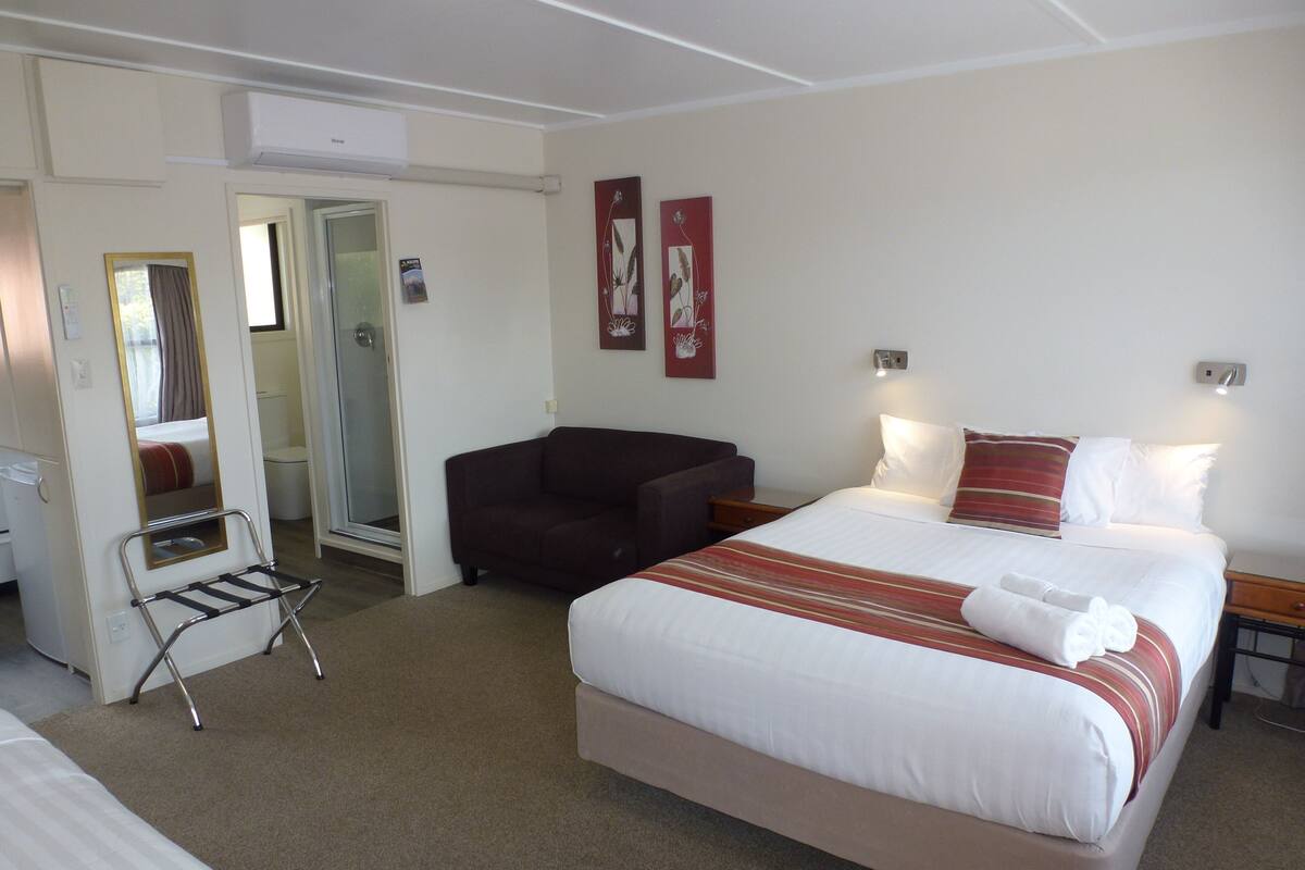 A hotel room with a bed, a chair, a small table, a mirror, and two wall-mounted lights.
