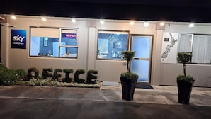 A hotel entrance with a 'NO VACANCY' sign, a 'WELCOME' sign, and the word 'OFFICE' spelled out with plants. - ASURE Adcroft Motel (Ashburton)