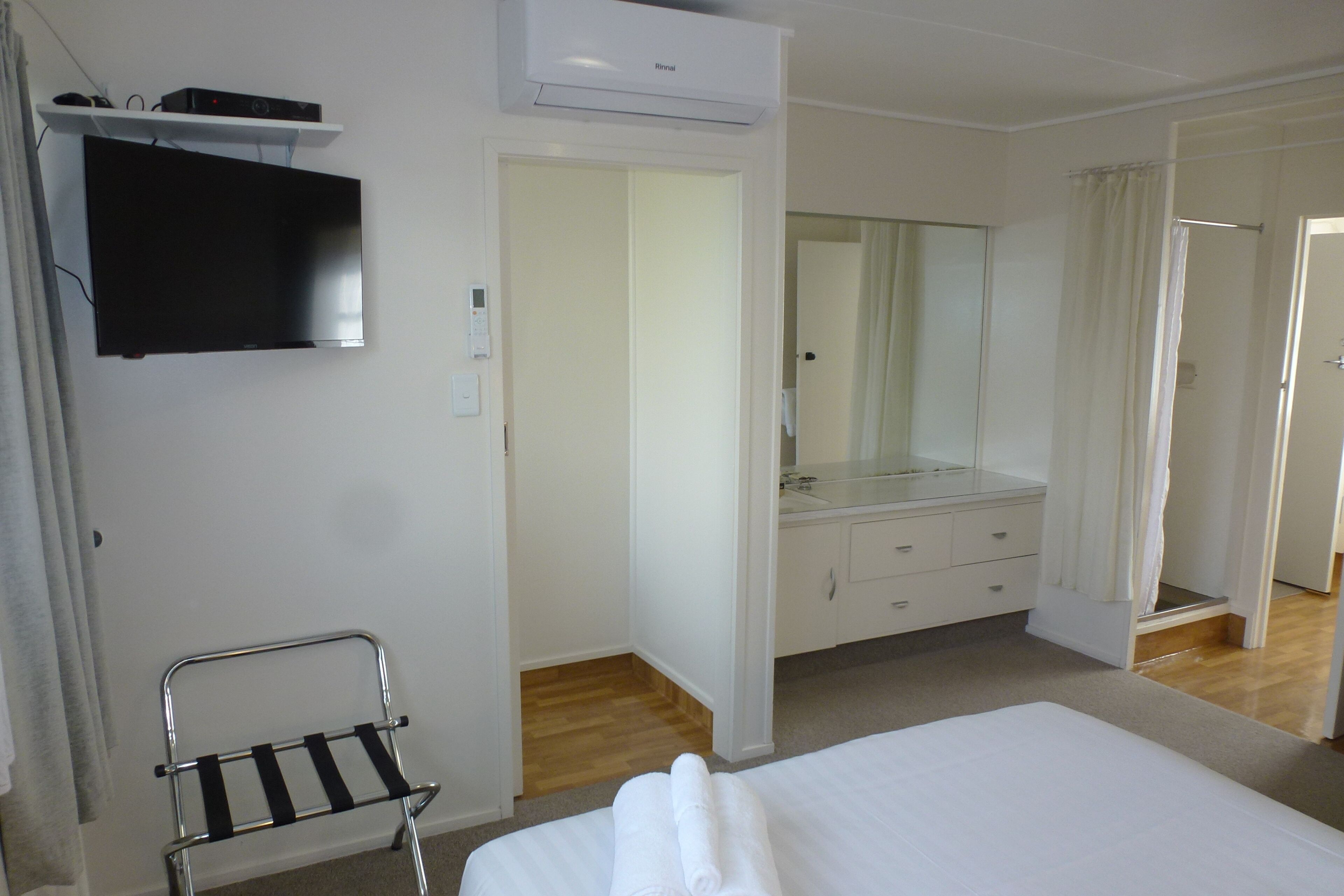 Ein Hotelzimmer mit Bett, einem an der Wand befestigten Fernseher, einem Spiegel über dem Schminktisch und einer Duschkabine.