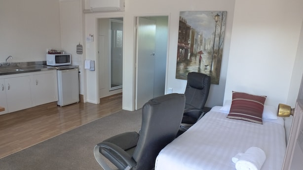 A hotel room with a bed, a chair, a microwave, a sink, and a painting on the wall. - ASURE Adcroft Motel (Ashburton)