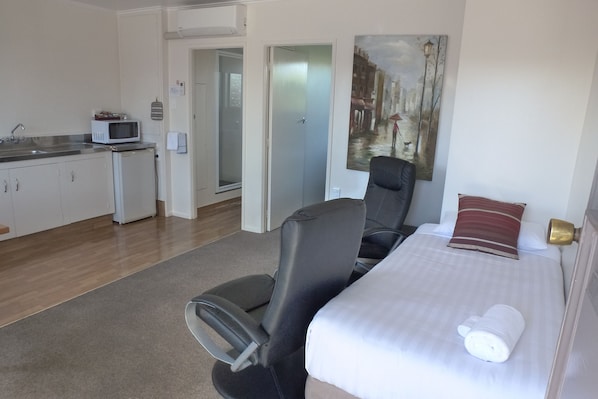 Una habitación de hotel con cama, una silla, microondas, lavabo y un cuadro en la pared.