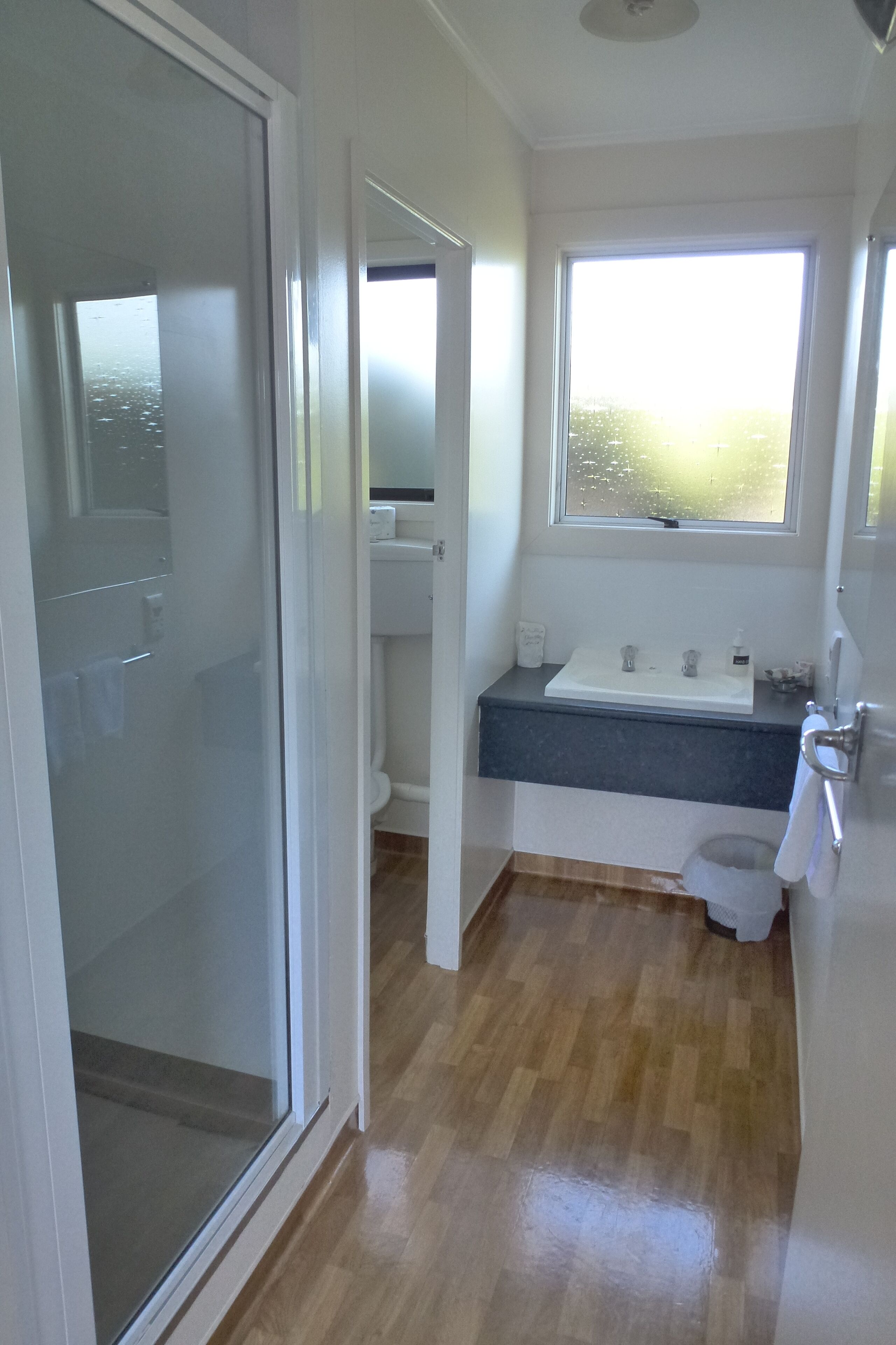 A bathroom with a glass shower door, a white sink with a dark countertop, and a window above the sink.