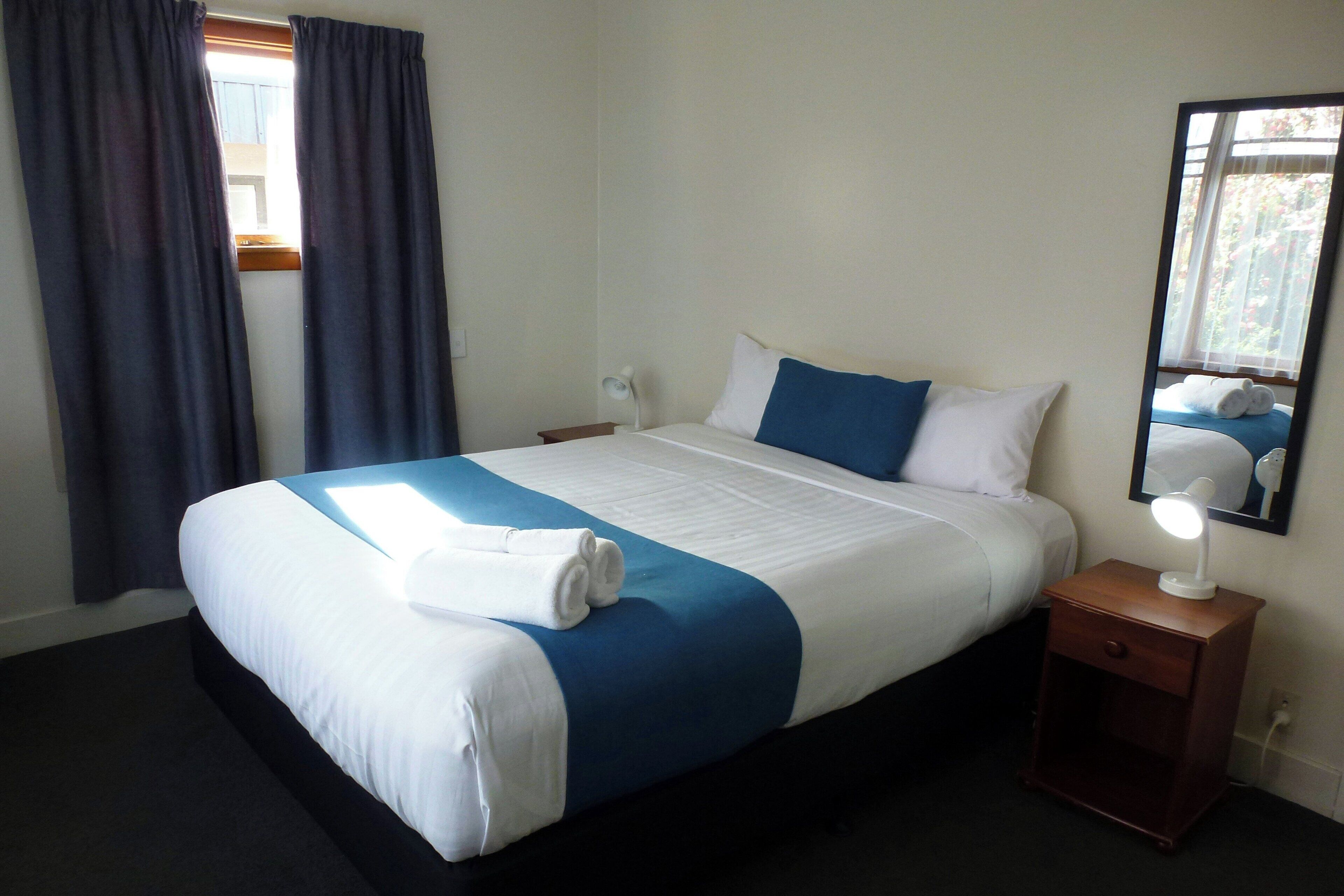 A hotel room with a large bed, a bedside table with a lamp, and a window with curtains.
