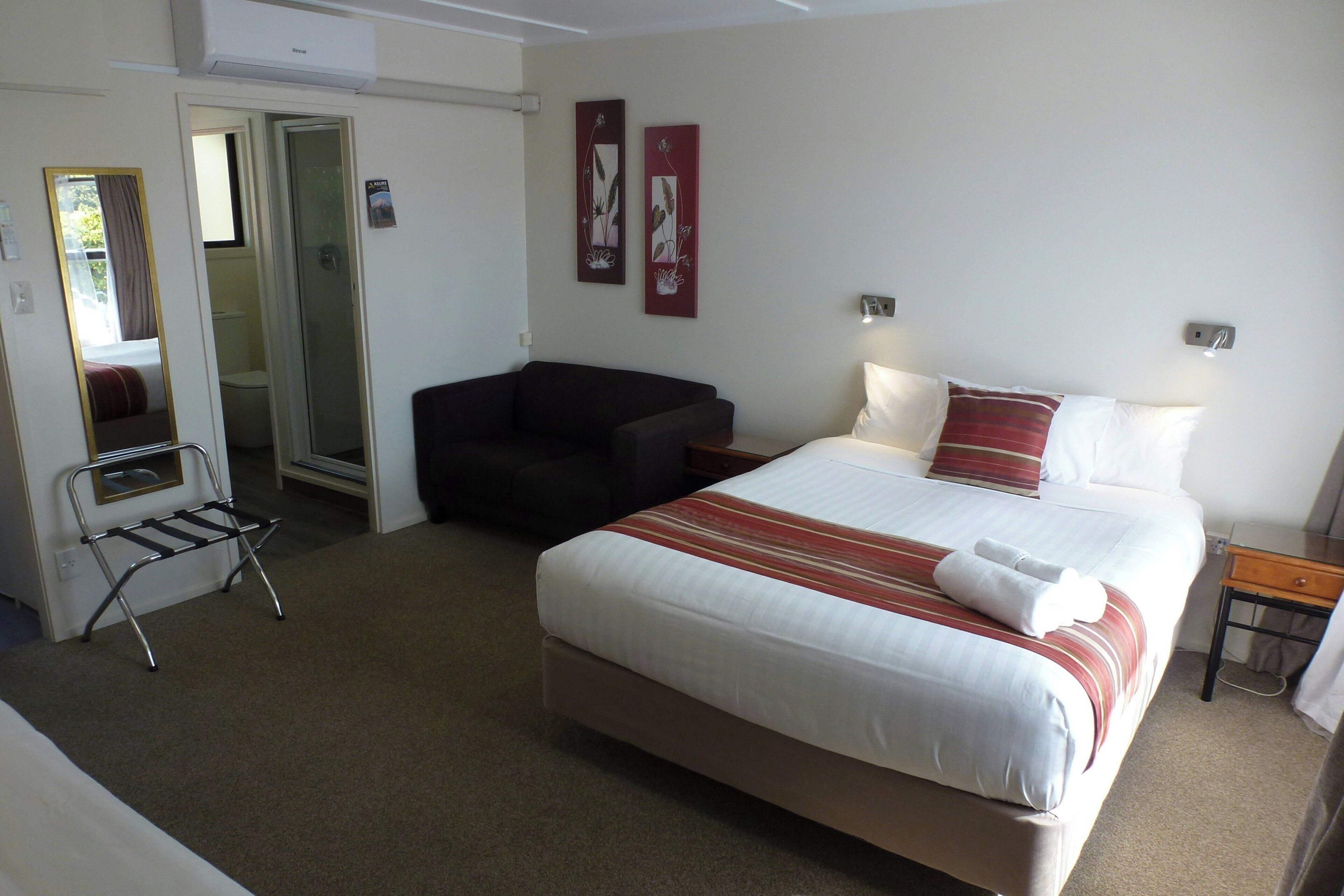 Ein Hotelzimmer mit Bett, Nachttisch, Lampe und einem Sessel.