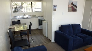 A compact kitchen with a dining area, a blue sofa, and a small table. - ASURE Adcroft Motel (Ashburton)