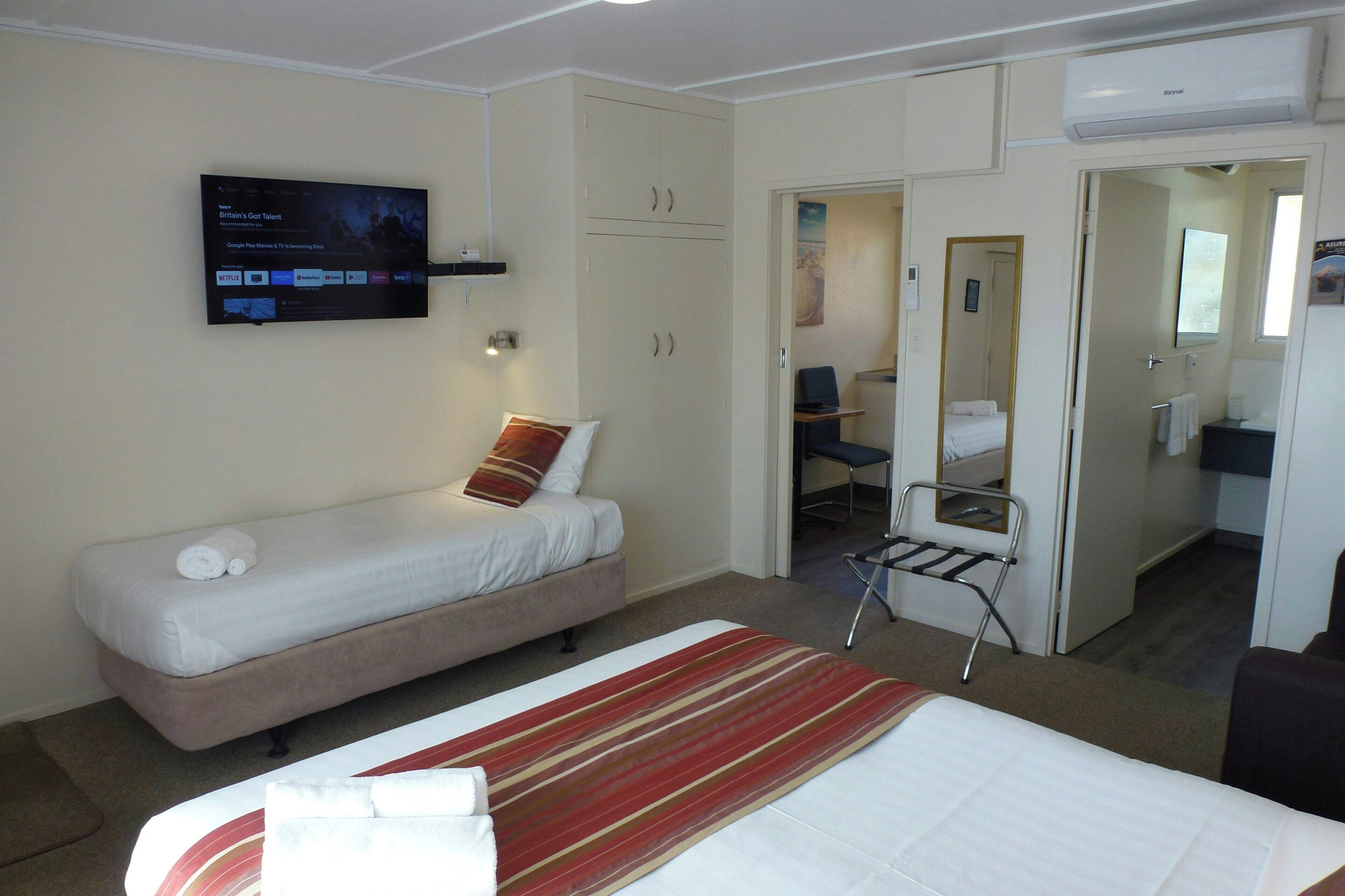 Habitación de hotel con una cama individual, escritorio, silla, televisor montado en la pared y armario.
