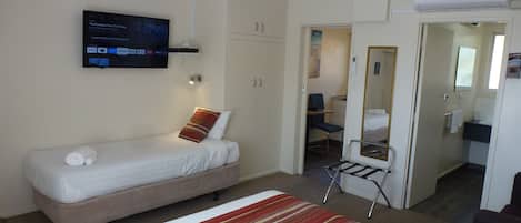 A hotel room with a single bed, a TV mounted on the wall, a wardrobe, and a bathroom visible through an open door.
