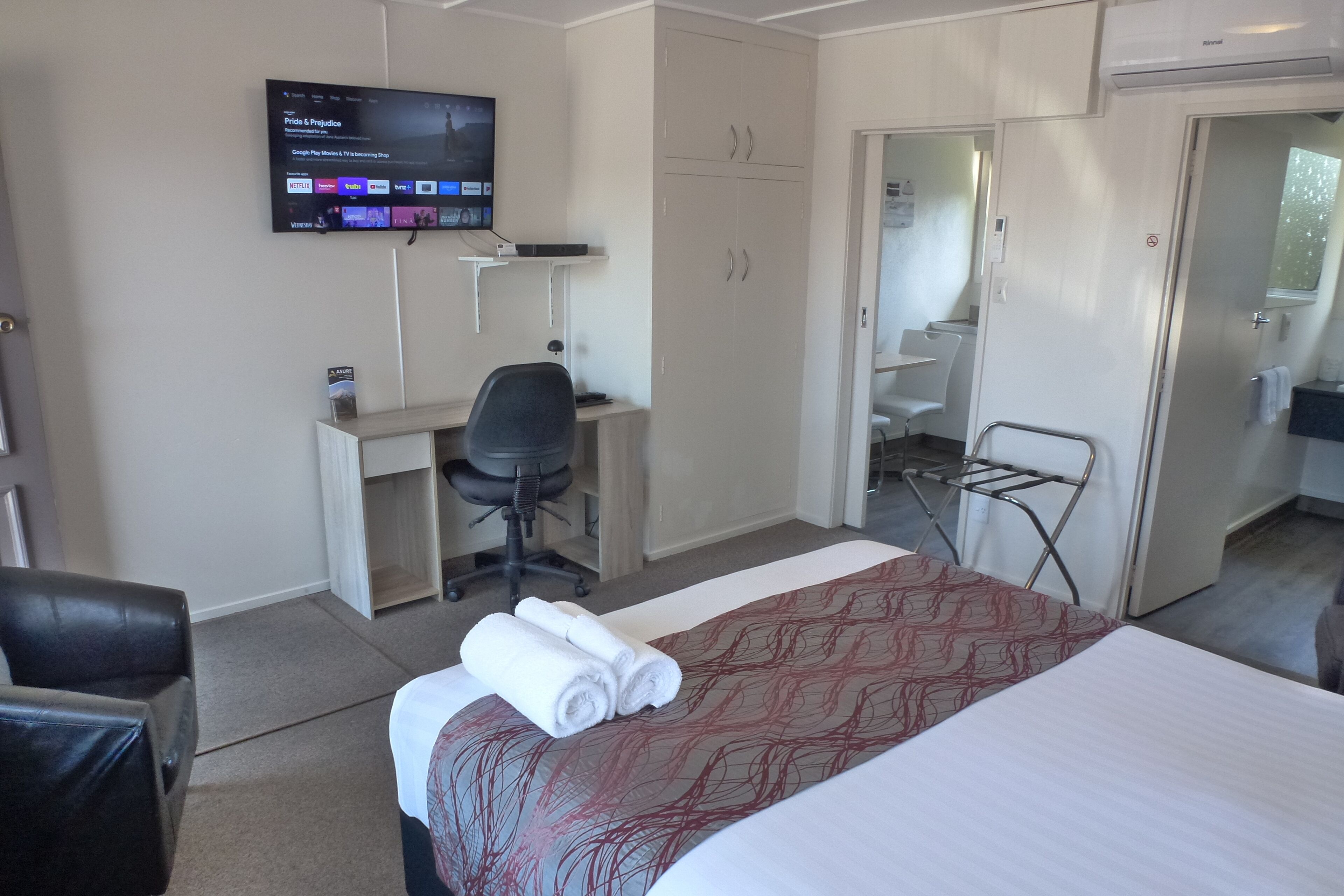A hotel room with a bed, a desk, a chair, a TV mounted on the wall, and a wardrobe.