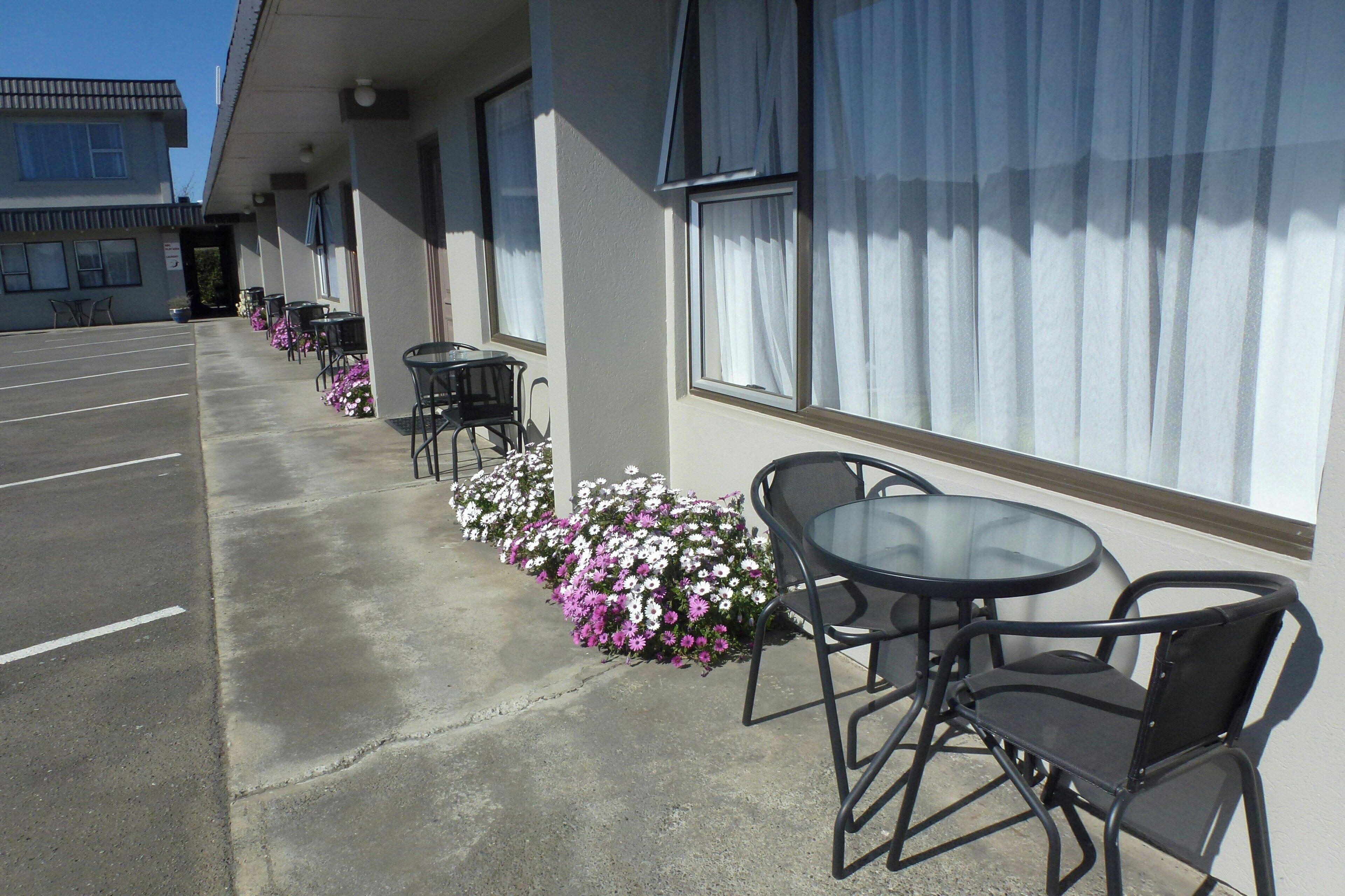 A hotel corridor with outdoor seating and flower beds.