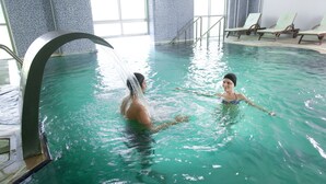 Uma piscina interior com água cristalina, um elemento aquático e espreguiçadeiras ao longo da borda.