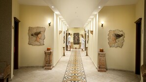 Um corredor de hotel com piso estampado, obras de arte decorativas nas paredes e uma estátua central.