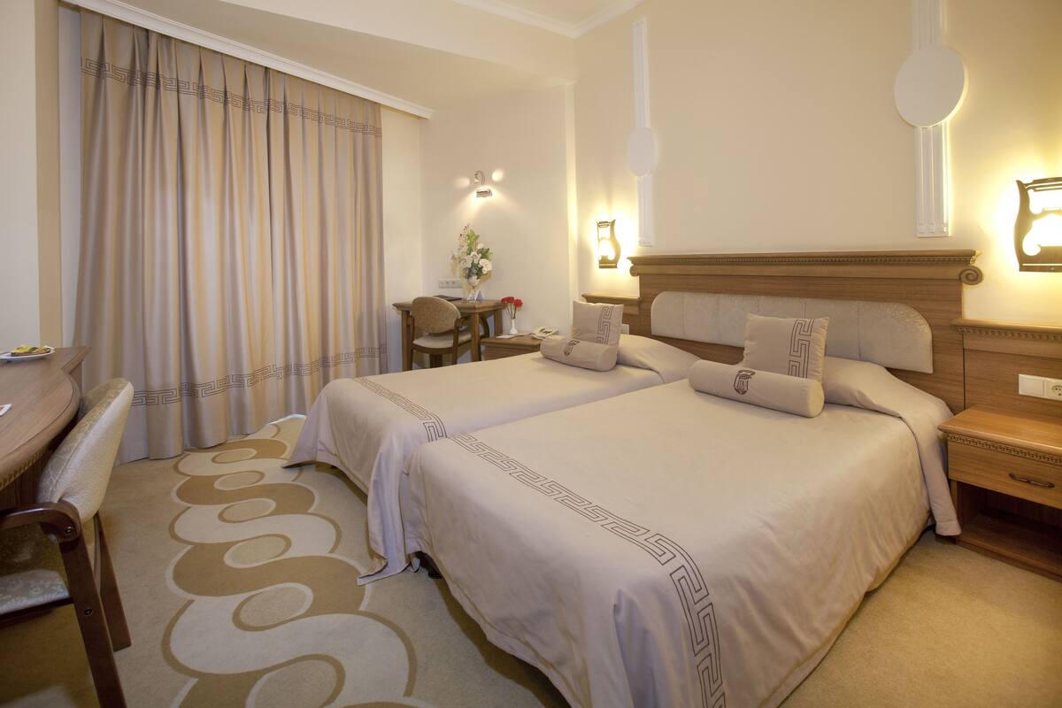 Een hotelkamer met twee bedden, een bureau, een stoel en een tafeltje met een bloevas.