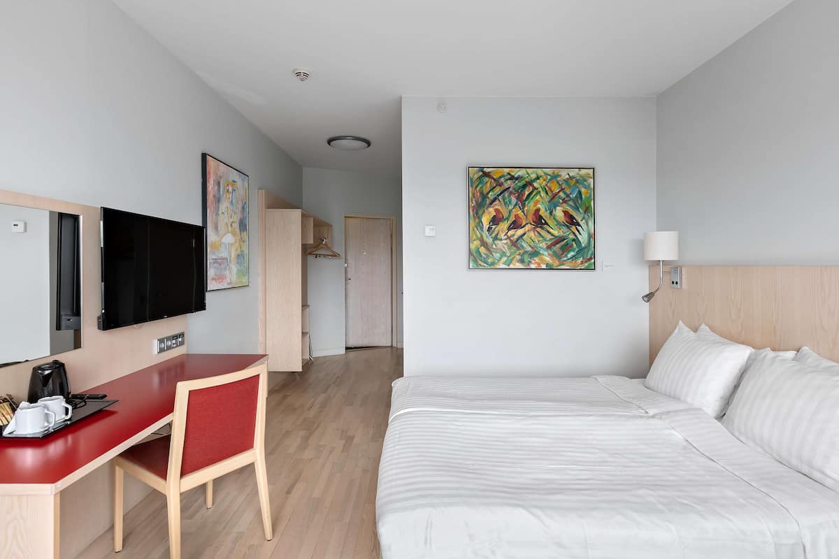 Une chambre d’hôtel comprenant un lit, un bureau avec une chaise, une télévision et des œuvres d’art accrochées aux murs.