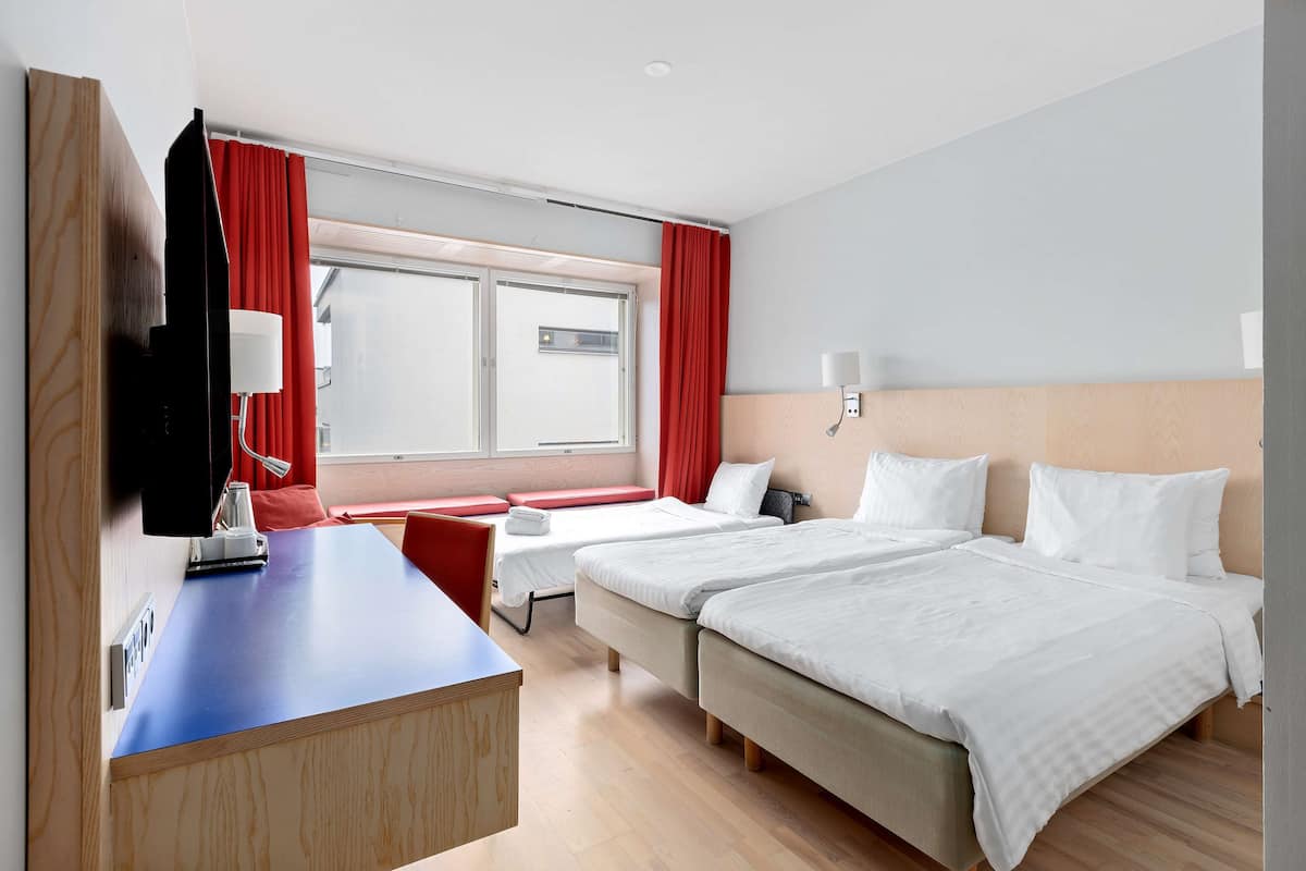 Une chambre d’hôtel avec deux lits, un bureau, une télévision et une fenêtre avec des rideaux rouges.