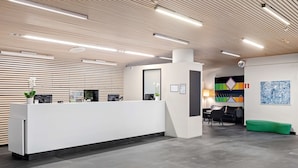 Un área de recepción moderna con un mostrador blanco, un banco verde y un cuadro abstracto de colores en la pared.