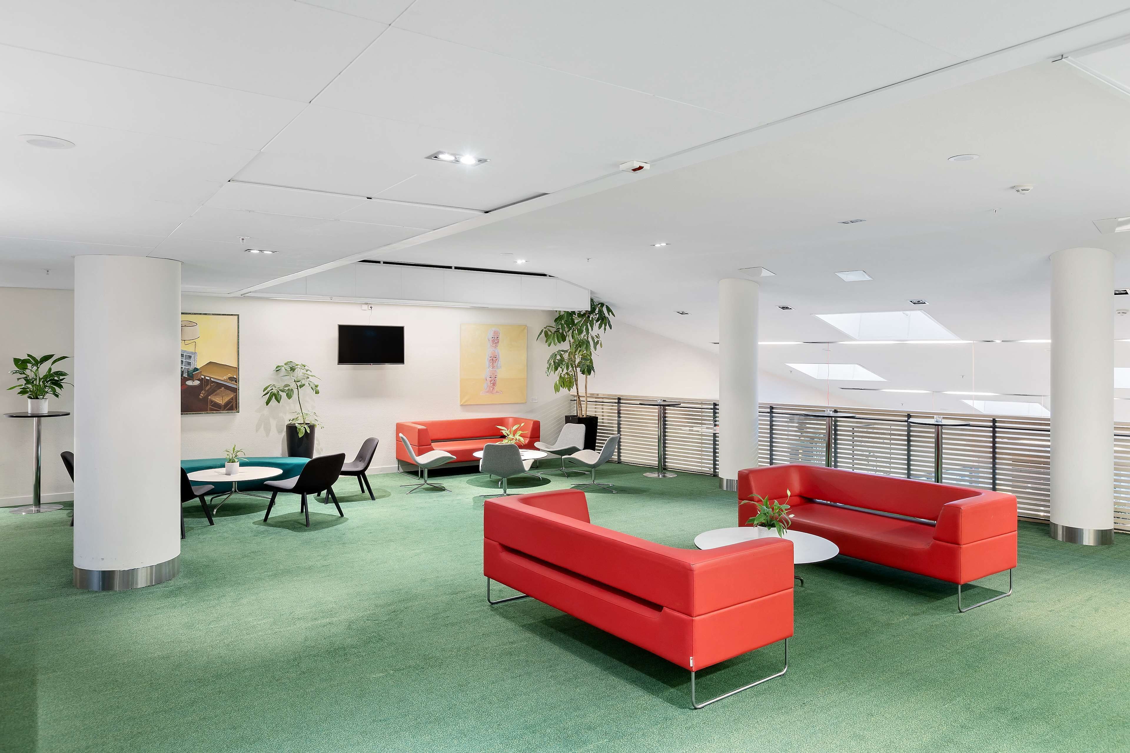 A modern office space with green carpet, red sofas, and a round table.