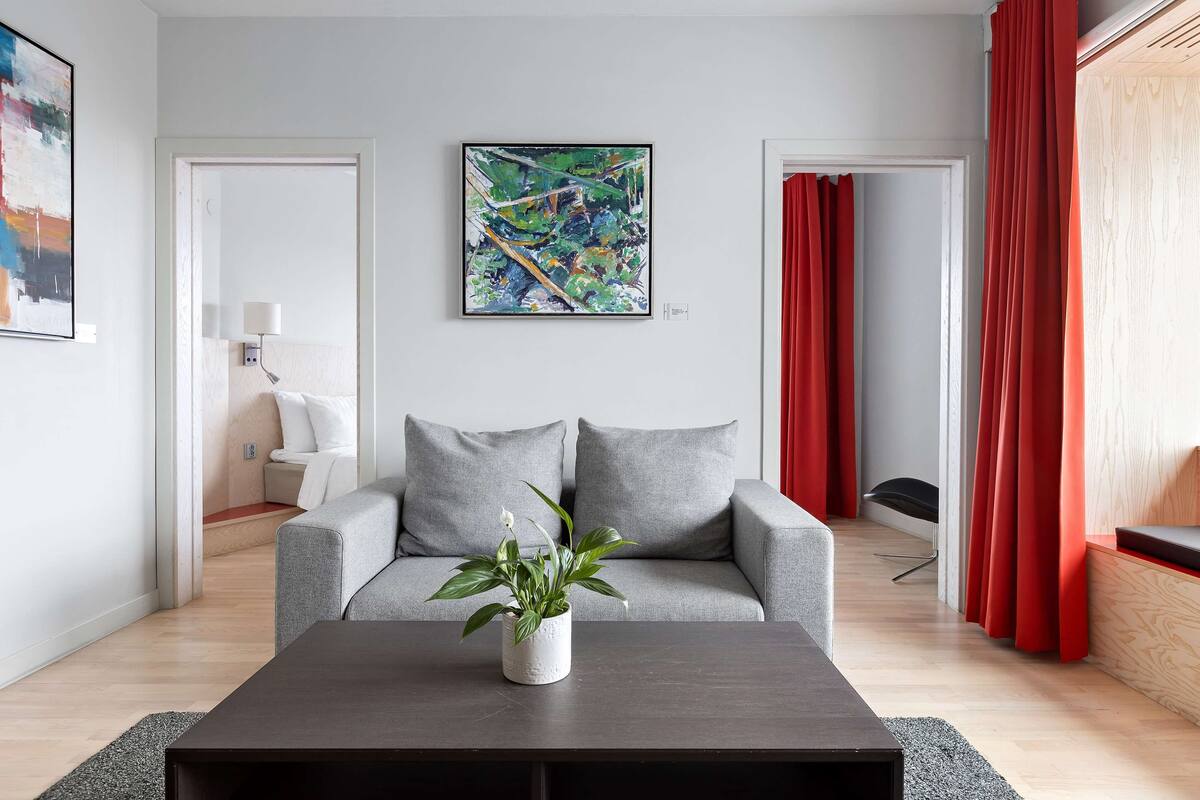 Un salon moderne avec un canapé gris, une table basse agrémentée d’une plante et un tableau abstrait aux couleurs vives accroché au mur.