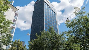 Un moderno edificio de gran altura con fachada de vidrio, rodeado de árboles bajo un cielo azul despejado.