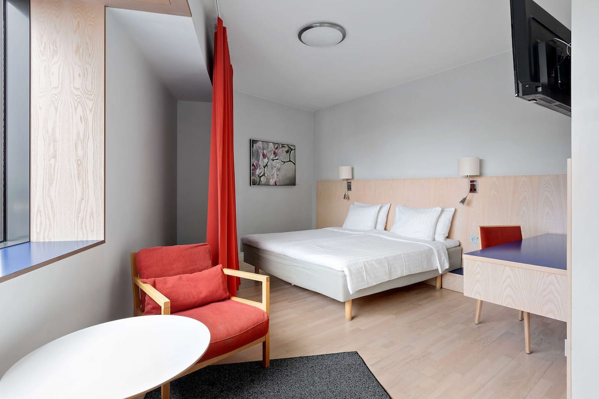 Une chambre d’hôtel moderne équipée d’un lit, d’un bureau, d’une chaise et d’un téléviseur fixé au mur.