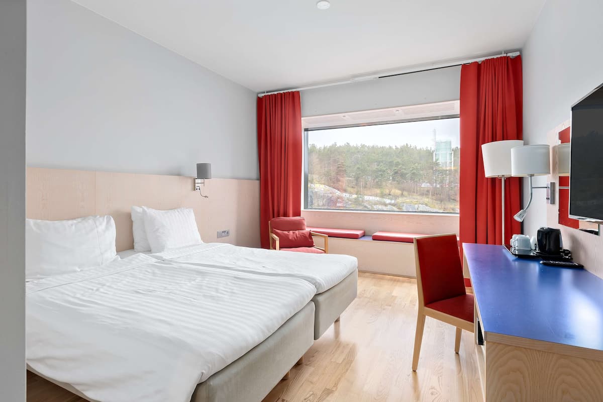 Une chambre d’hôtel avec un grand lit, un bureau avec une chaise, une télévision et une fenêtre avec des rideaux rouges.