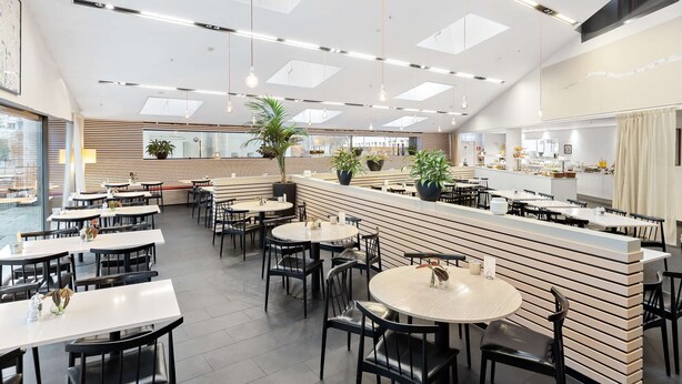 Un restaurante moderno con varias mesas y sillas, una barra y plantas en macetas.