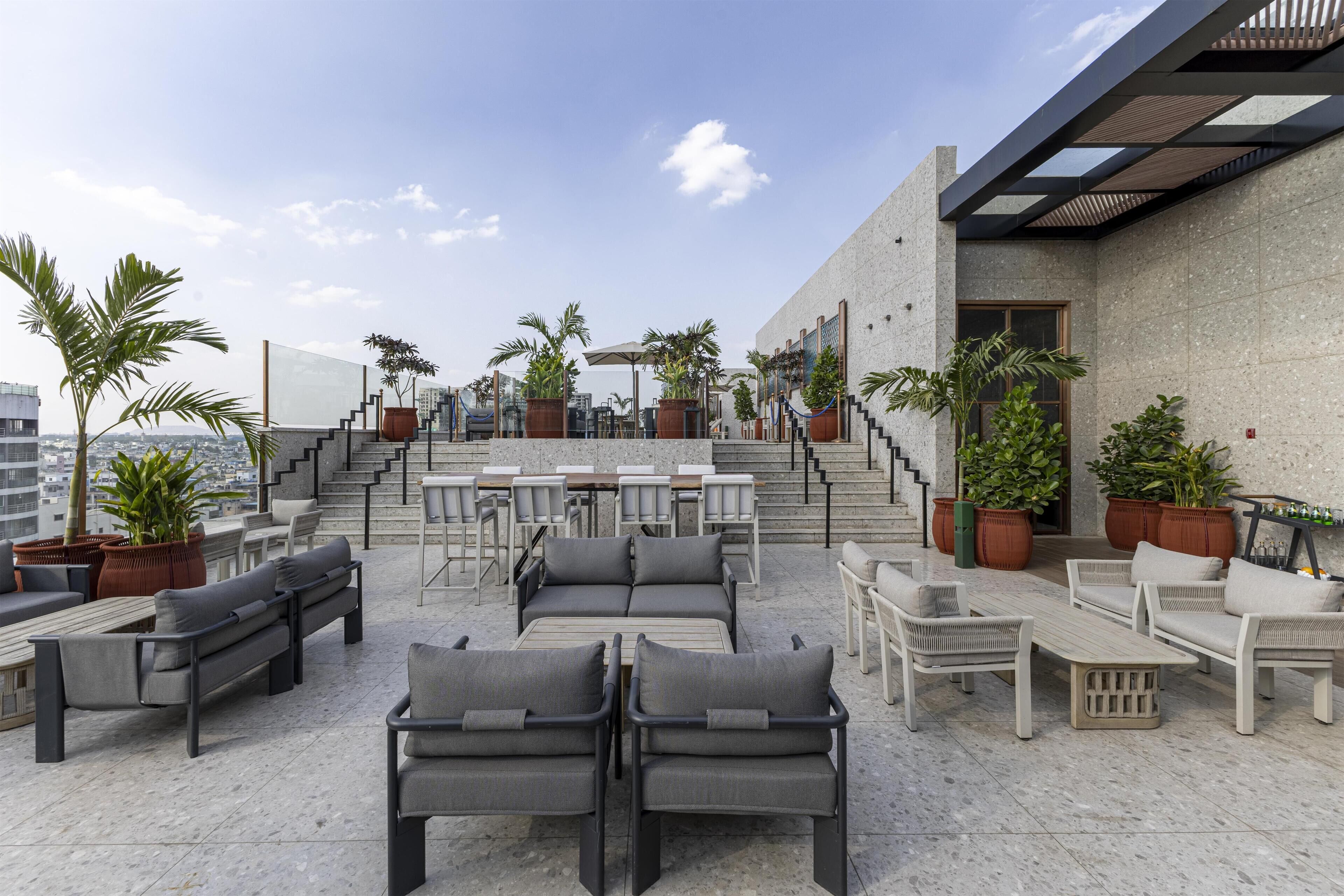 A rooftop terrace with outdoor seating, potted plants, and a staircase leading to an upper level.