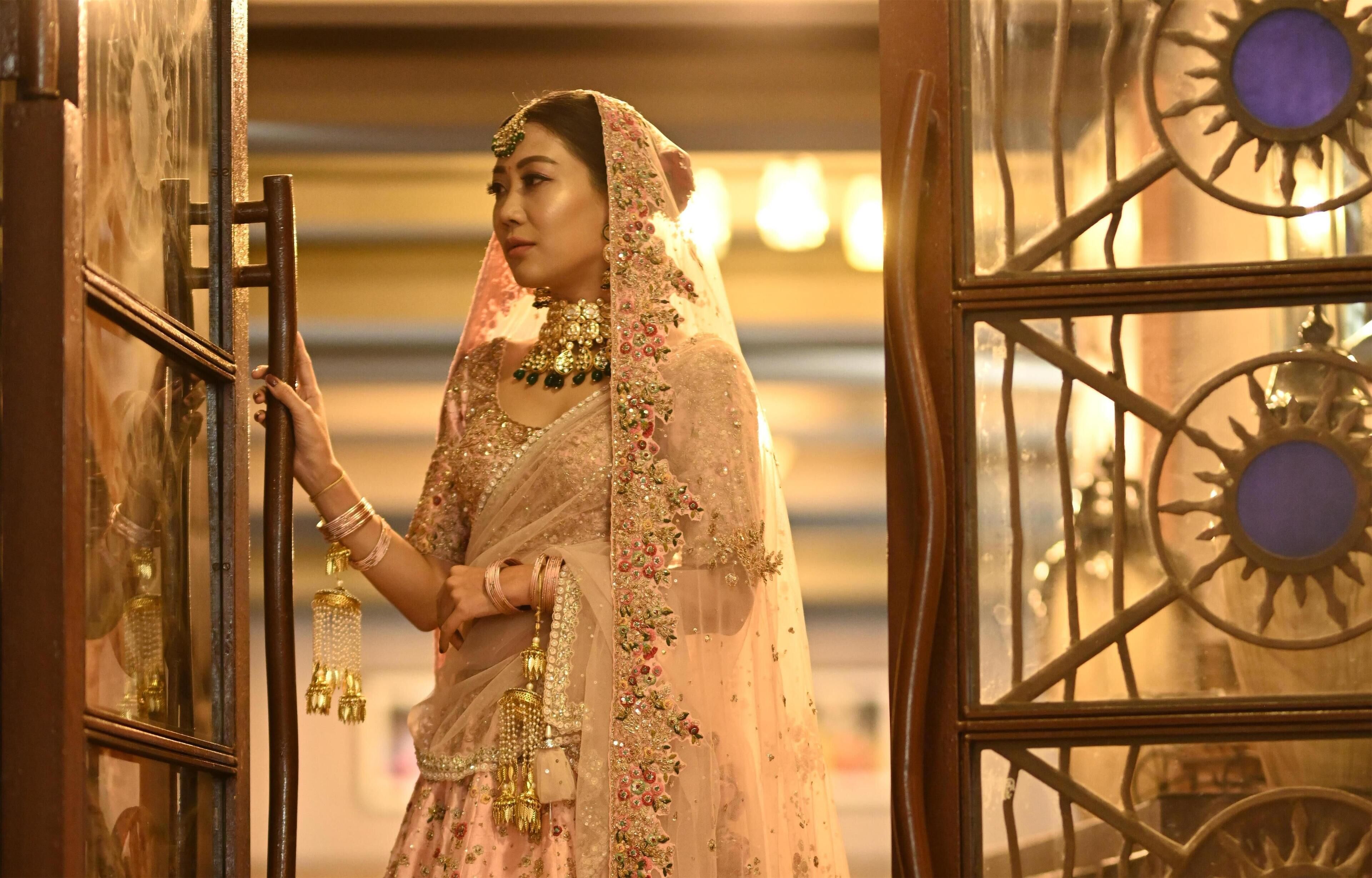A person in traditional attire standing at a door with a decorative metal design.