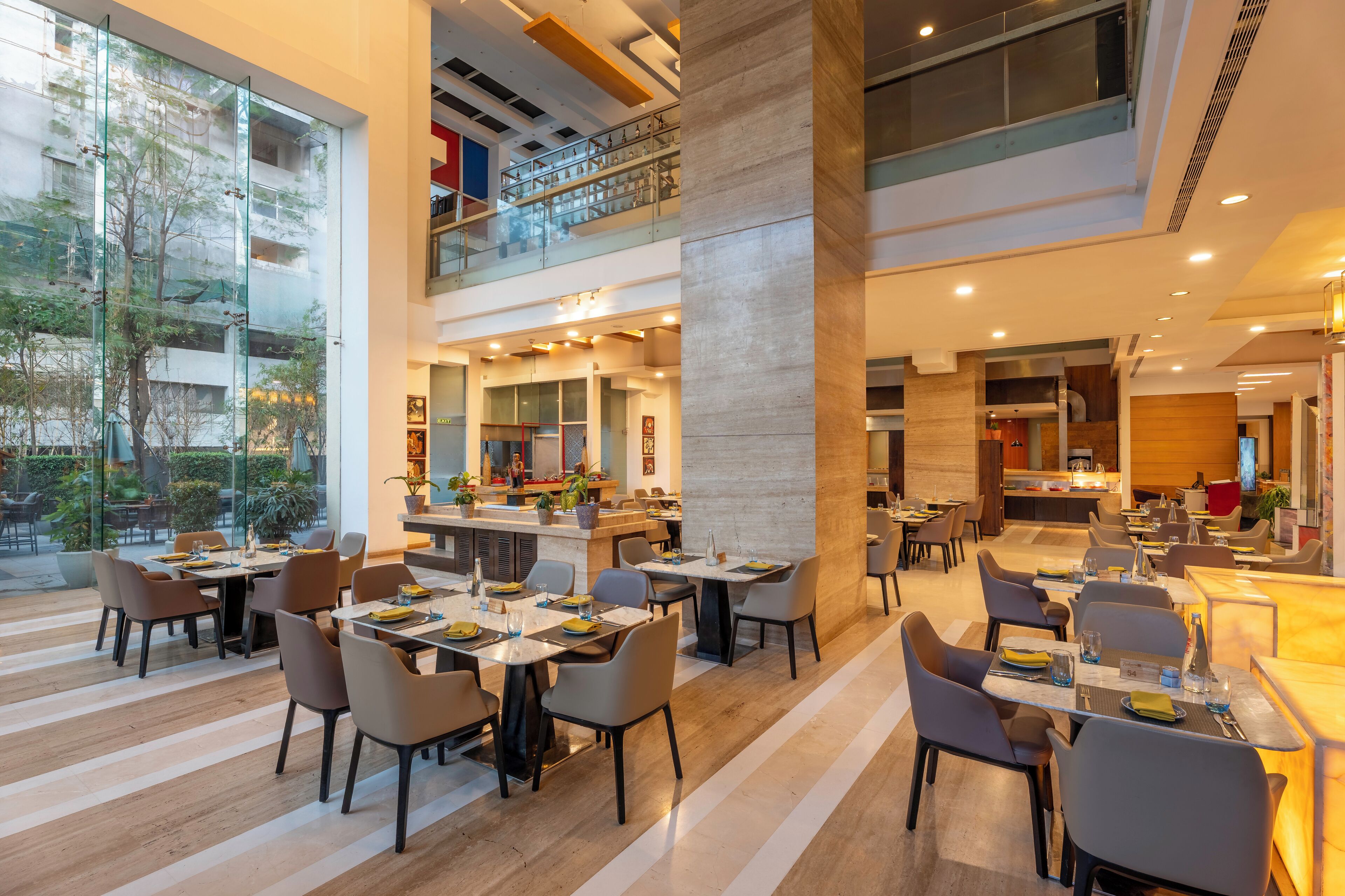 Un amplio vestíbulo de hotel con varias zonas de comedor, un bar central y vistas al exterior.