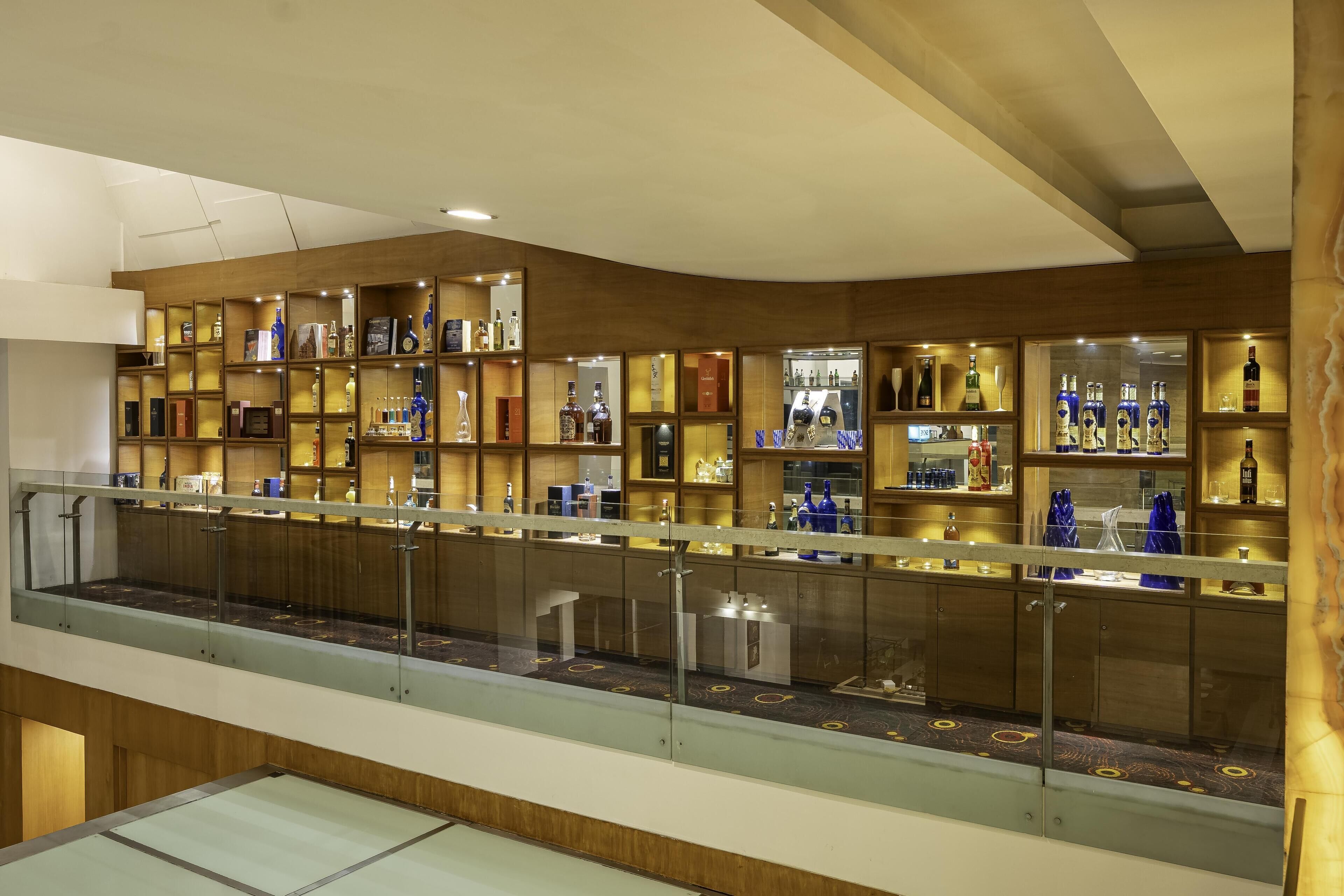 Un espace bar avec des étagères remplies de bouteilles et de verres, une rambarde en verre et un plafond en bois.
